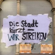 Tuch außen an der Fassade des Frauennotruf mit den Worten: Die Stadt kürzt - WIR STREIKEN